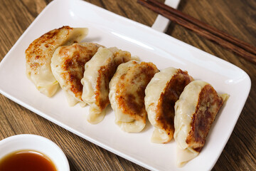 A serving of freshly cooked gyoza dumplings. This is an ideal appetizer or meal eaten with chopsticks. Captured with natural light and presented on a wooden background.