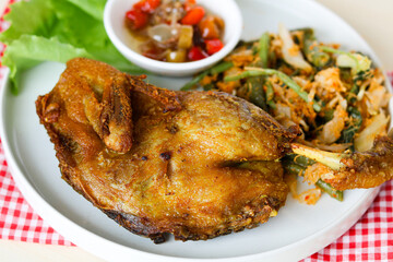 Closeup of an authentic meal of fried duck (bebek goreng) with a side of blanched vegetables (urap) and a bowl of spicy sambal matah.