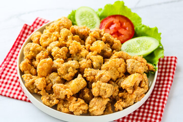 A plate of crispy, bite-sized salted egg chicken, garnished with fresh slices of cucumber and tomato.