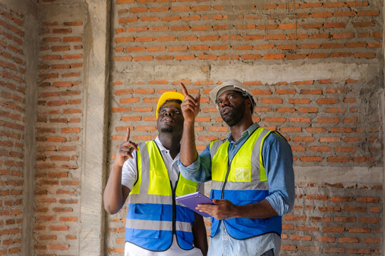 Black engineer and construction worker checking and planning work on his tablet at construction site.