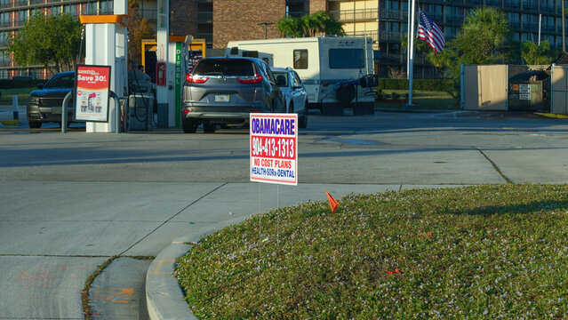 Obamacare sign advertising health insurance plans at gas station with vehicles parked nearby, promoting affordable healthcare options for the community