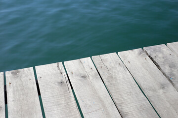 Fototapeta premium Wooden pier planks extending over calm blue water.