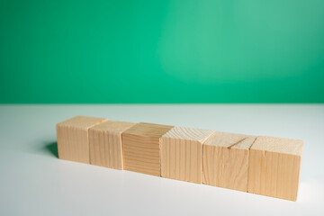 Wooden cubes aligned on white table with green background representing minimalism, design, and creativity