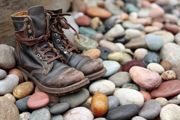 Vintage leather boots resting on colorful pebbles in nature, showcasing worn-out design and rustic charm of footwear