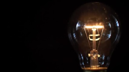Close-up of a glowing incandescent light bulb against a dark background, symbolizing innovation, ideas, and energy solutions. - Powered by Adobe
