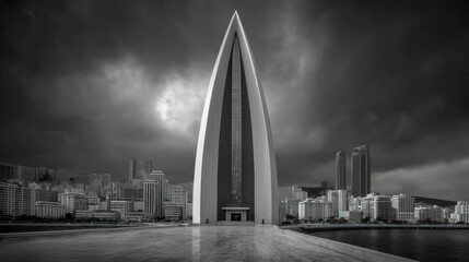 Modern architectural landmark with sharp spire against dramatic cloudy sky overlooking a cityscape and water