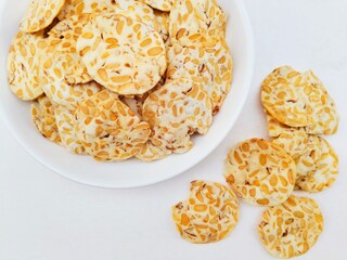 Close-up of tempeh chips in a white plate on a white background.