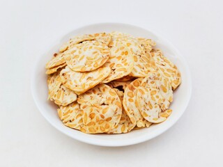 Tempeh chips in a white plate on a white background. High angle view. 