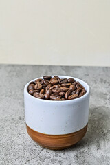 Side view roasted coffee beans in the ceramic glass or mug. Little, mini. Isolated on gray or gray cement background. Close up, front. Copy space, empty, free, negative, design, text. Potrait photo.