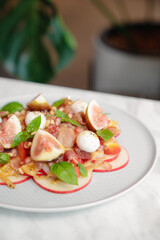 Fresh fig and apple salad with mozzarella cheese, pomegranate, and herbs on white plate