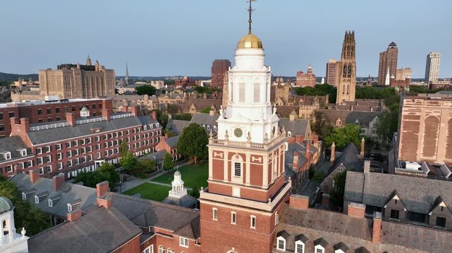 Aerial flight over Davenport college with courtyard and church tower with golden cupola. Passing by shot. Harness. Tower of Yale university in background. New Haven, Connecticut at sunset.