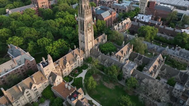 Harkness Tower at Yale old campus university of New Haven. American City in Connecticut at sunset. Summer day with green trees. Industrial waterfront In distance. Aerial tilt up wide shot.