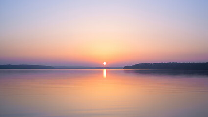 Obraz premium Serene sunset over calm water with soft pastel colors reflecting the sky and distant horizon creating a peaceful natural landscape