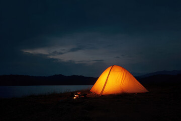 Glowing tent and campfire under dramatic night sky create serene atmosphere