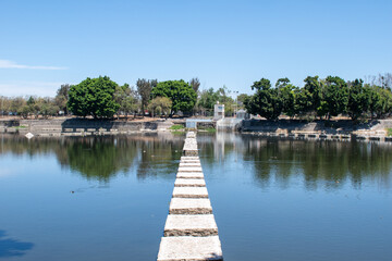 Fototapeta premium Long stone path stretches across a calm body of water at Parque Independencia El Dean in Guadalajara, Mexico under a clear sky