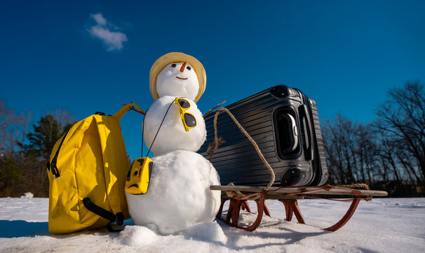 Snowman with luggage ready for holiday trip. Winter vacation starts with snowman. Funny snowman holding travel bag outdoors. Festive snowman tourist on winter adventure. New Year journey.