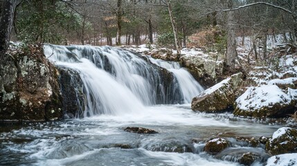 Fototapeta premium A cascading waterfall flows over moss-covered rocks in a snowy forest setting. The water is clear and white, creating a dynamic and visually appealing scene. 
