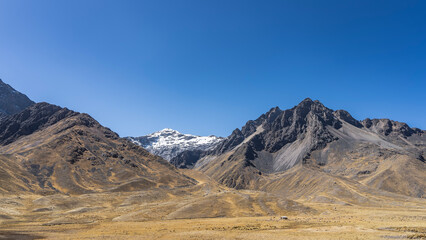 Beautiful mountain landscape. Black and brown slopes, devoid of vegetation. A snow-covered peak against a clear blue sky. The Andes Mountains. Highlands of Peru