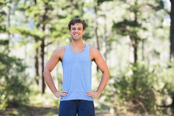 Fototapeta premium Man running on forest trail in blue sleeveless shirt and navy shorts under sunlit pine canopy