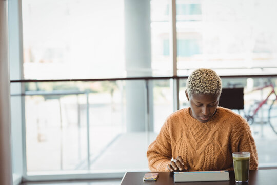 African American woman focusing on tablet while sitting at cafe with green smoothie, copy space - Powered by Adobe