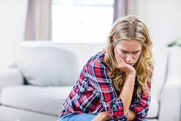 Fototapeta premium Woman leaning forward on sofa in living room wearing plaid shirt and jeans, copy space