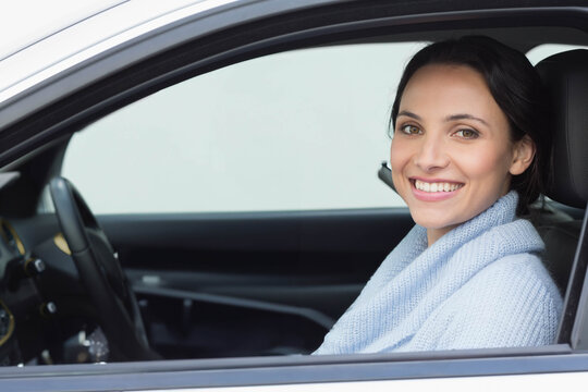 Woman gripping steering wheel wearing light blue sweater and smiling inside parked car, copy space