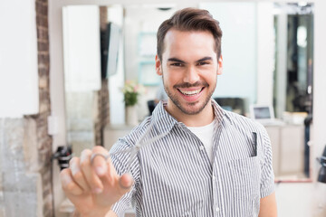 Male stylist holding scissors and comb in pocket while styling hair at modern salon mirror