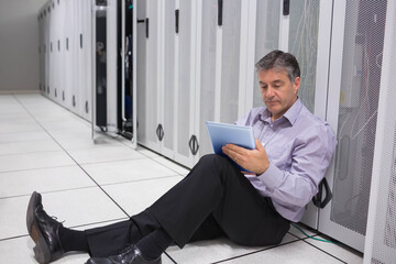 Senior man in dress clothes leaning against server rack, checking tablet at data center, copy space