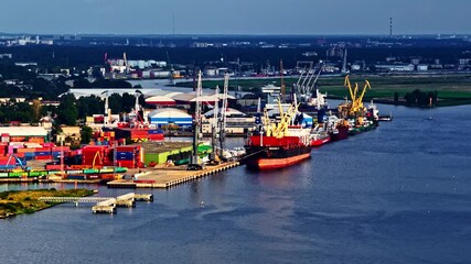 Wide aerial of container ships docked at a bustling seaport lined with colorful cargo containers and cranes over calm blue waters - Powered by Adobe