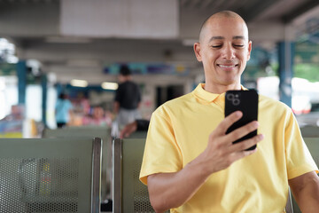 Hispanic bald tourist man waiting for bus and using phone at station platform