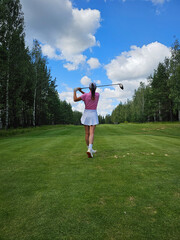 Golf player swings club on lush green fairway under vibrant blue sky with fluffy clouds
