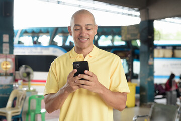 Hispanic bald tourist man waiting for bus and using phone at station platform