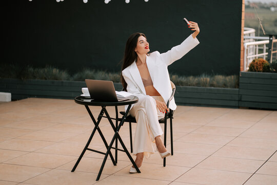 Professional woman enjoying a selfie while working on a rooftop terrace in the evening