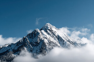 Obraz premium Isolated mountain with snow-capped peak emerging among low clouds, photographed from afar against empty sky, impression of majesty and minimalism