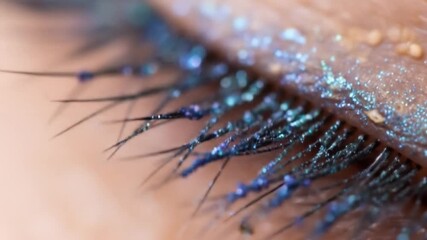 Elegant eye makeup demonstration featuring shimmering blue glitter on eyelashes and eyelid,