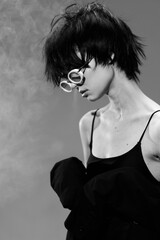 Black and white portrait of a young woman with short hair and round glasses wearing a dark top against a textured background.