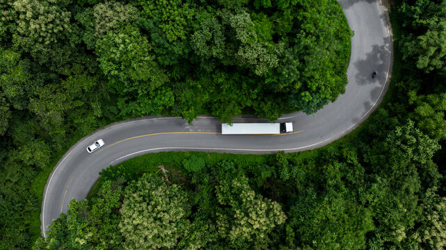 Aerial view semi truck trailer cargo on mountain curve road, Semi truck trailer cargo business logistic transportation on green forest road curve, Semi truck delivery asphalt road green forest tree. - Powered by Adobe