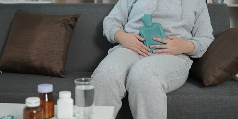 Home remedy. Young woman using hot water bottle for stomach pain relief.
