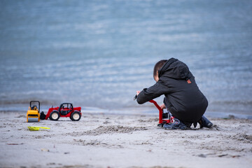 Child playing with toy trucks on sandy beach by the sea