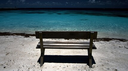 A wooden bench sits on a sandy beach, facing the ocean.