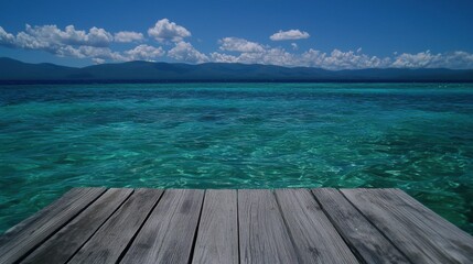 A wooden dock extends into a turquoise ocean, with a mountain range in the distance.