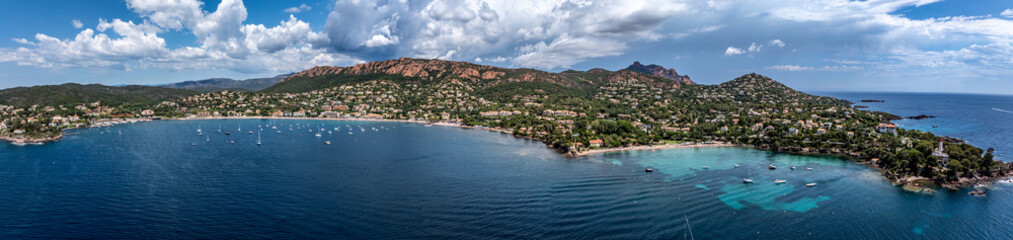 panoramic aerial landscape view of French Riviera coastline along Agay Bay in Saint-Raphaël with Plage d'Agay and Plage de La Baumette, many boats anchored in bay, wooded hilly landscape in background