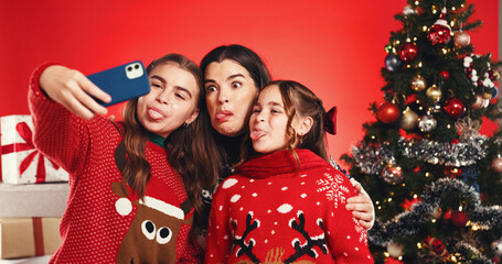 Christmas, mother and children with selfie in studio for festive season, tongue out or bonding. Goofy family, people and photography on red background for winter holiday, xmas memory and celebration