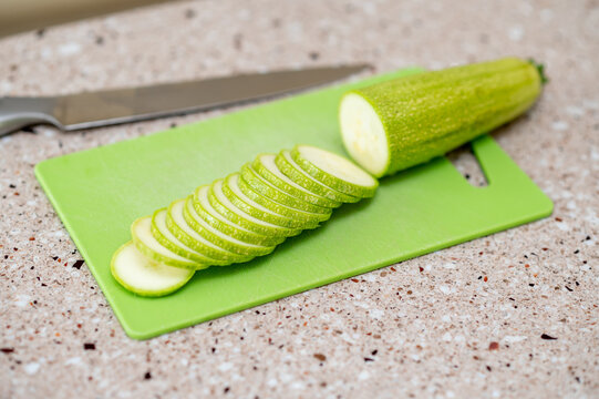 Fresh zucchini being sliced on a green cutting board in kitchen, concept: healthy cooking preparation