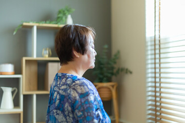 室内の床に座って目を閉じ、瞑想をする60代の日本人シニア女性 横顔 上半身