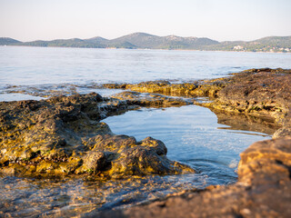 Low angle view of limestone rocks forming a small natural pool by the Adriatic Sea in Biograd na Moru, Croatia, with calm water and peaceful sunrise atmosphere.