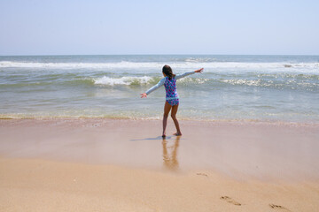 Girl stretches arms while standing in shallow surf