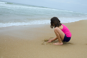 Girl draws in wet sand while sitting by the ocean
