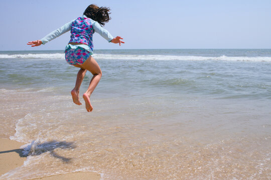 Girl leaps joyfully over foamy waves on beach shore