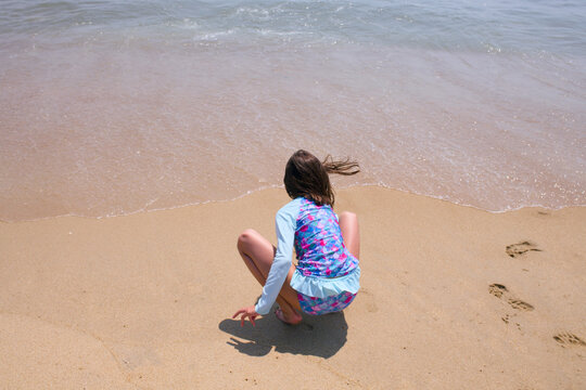 Young girl plays in the sand at the edge of the beach